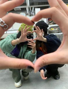 two people holding their hands up in the shape of a heart with one person taking a photo