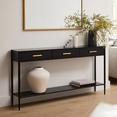 a white vase sitting on top of a wooden table next to a black and white shelf