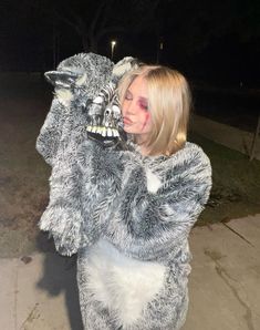 a woman dressed as a wolf with makeup on her face and arms, holding onto the back of a stuffed animal