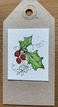 a christmas card with holly leaves and berries on it, hanging from a wooden hanger