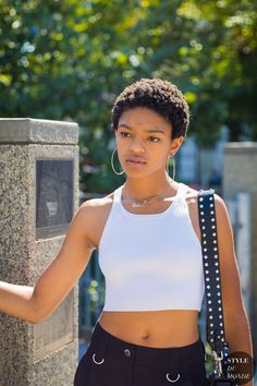 a woman in white top and black pants standing next to a stone wall with her hand on her hip