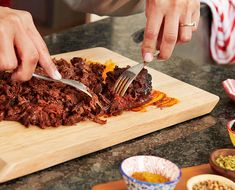 a person cutting meat with a knife and fork on a cutting board next to other food