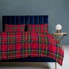 a bed with a red and green plaid comforter next to a night stand on a white floor