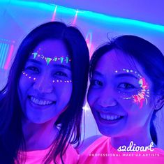 two girls with face paint smile for the camera in front of neon lights and balloons