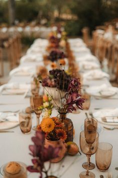 a long table is set with glasses, plates and vases filled with colorful flowers