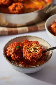 a bowl filled with meatballs and sauce on top of a white table next to a pan