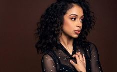 a woman with curly hair wearing a black dress and holding her hand on her chest