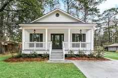 a small white house with porch and steps leading up to the front door, surrounded by trees