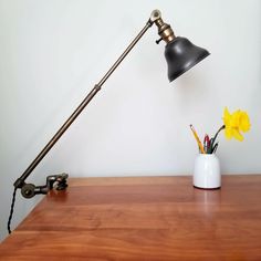 a desk lamp sitting on top of a wooden table next to a vase with flowers