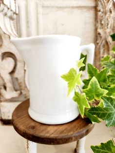 a white vase sitting on top of a wooden table next to a potted plant