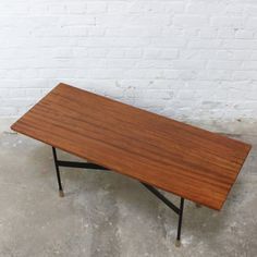 a wooden table sitting on top of a cement floor next to a white brick wall