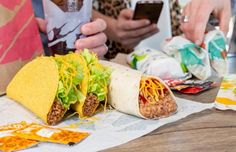 two people sitting at a table with food and cell phones in front of them,