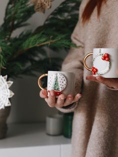 a woman holding two coffee mugs in her hands, one with a christmas tree on it