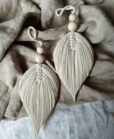 two white earrings with wooden beads on top of a bed covered in gray linens