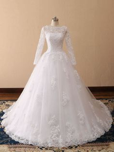 a white wedding dress with long sleeves and flowers on the skirt is sitting on a rug