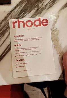 a person holding up a menu on top of a marble counter with red lettering that reads rhode