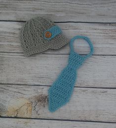 two crocheted hats and a blue tie on a wooden surface