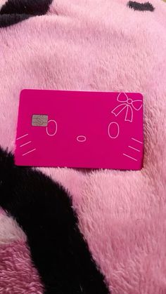 a pink hello kitty credit card laying on top of a black and white cow print blanket