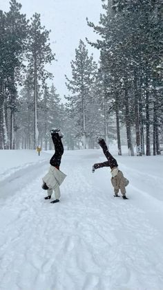 two people doing tricks in the snow near trees