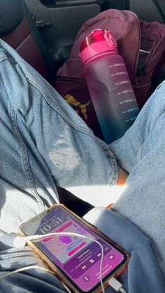 a person sitting in the back seat of a car with their cell phone and water bottle