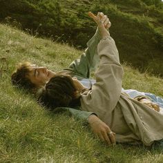 two people laying in the grass with one pointing at something while the other looks up