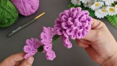 a person holding a crocheted flower in their hand next to some yarn and flowers