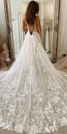 a woman standing in front of a mirror wearing a wedding dress with flowers on it