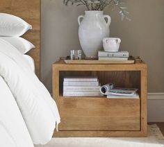 a white vase sitting on top of a wooden shelf next to a bed with pillows