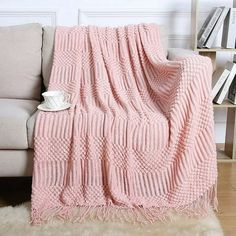 a pink knitted blanket sitting on top of a couch next to a book shelf