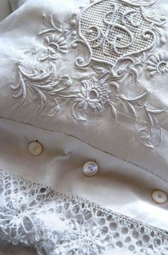 an embroidered pillow with buttons and lace on the bottom is sitting on a bed sheet