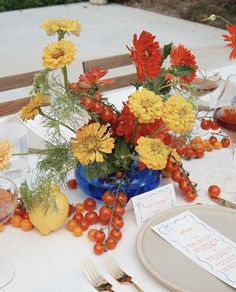 an arrangement of flowers and fruit on a table set for a formal dinner or party