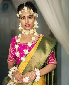 a woman in a pink and yellow sari with white flowers on her head is posing for the camera