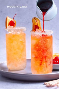 two glasses filled with drinks sitting on top of a white plate next to an orange slice