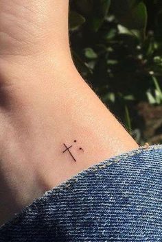 a small cross tattoo on the foot of a woman's ankle, with leaves in the background