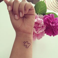 a person with a small tattoo on their wrist holding a pink flower in front of them