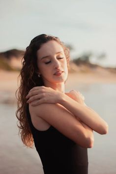 a woman standing on the beach with her arms folded over her chest and eyes closed