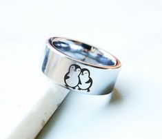 "**Please note any of our engraving designs can be engraved on any ring style within our shop! Send us a message to get started☺️ This is an adorable penguin ring! A cute penguin couple being smitten with one another :D This listing is 8mm be default, but you can request different in personalization before checkout. ABOUT OUR ENGRAVINGS Our engravings are 100% permanent and are produced with a state of the art laser engraving machine. The color of our engravings are 100% natural, we do not use a Silver Laser Engraved Rings As Gift, Anniversary Silver Rings With Laser Engraving, Stainless Steel Rings With Engraving Option For Wedding, Stainless Steel Wedding Rings With Engraving Option, Wedding Rings With Engraving Option In Stainless Steel, Cute Penguin Couple, Penguin Ring, Wedding Band Engraved, Penguin Bracelet