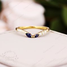 a gold ring with blue and white stones on it sitting on a box next to some flowers