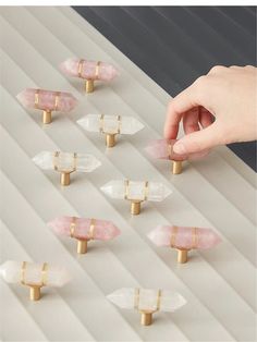 a person is picking up some small pink and white stones with gold pins on them