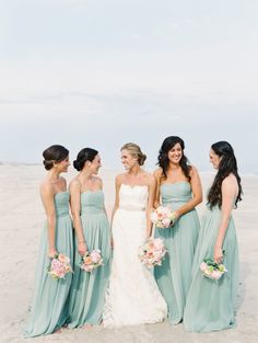 a group of women standing next to each other on top of a sandy beach in front of the ocean