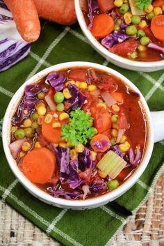 two white bowls filled with vegetable soup on top of a table