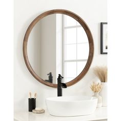 a round mirror hanging on the wall above a white sink and faucet in a bathroom