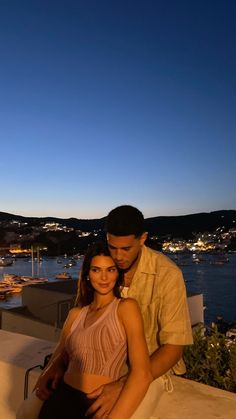 a man standing next to a woman on top of a roof near the ocean at night