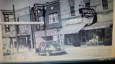 an old black and white photo of a car parked in front of a storefront