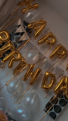 gold balloons and streamers with the word happy birthday spelled out in large letters on a white wall