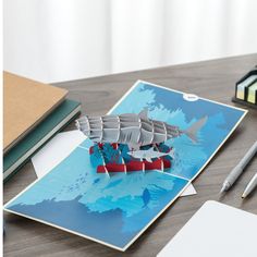 an origami model of a ship on a table with markers and pencils