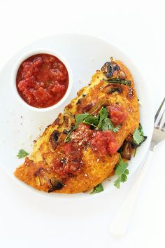 a white plate topped with an omelet next to a bowl of tomato sauce