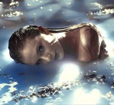 a woman is floating in the water with her hair blowing back and looking at the camera