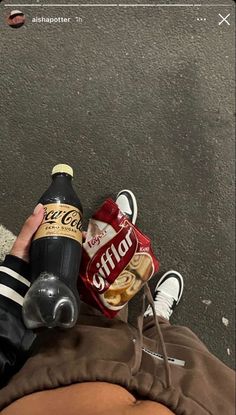 a person is holding a bottle of beer and some food on the ground next to them