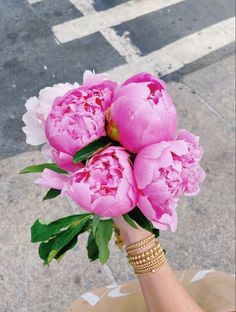 a bouquet of pink peonies is being held by a woman's hand